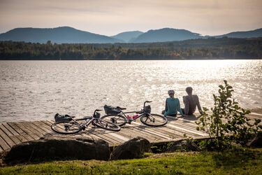 Zwei Radfahrer sitzen auf einem Steg am See bei Sonnenuntergang.